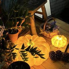 Yellow pumpkin-shaped portable table lamps with built-in battery on wooden surface, surrounded by plants and pine cones, from YH Lamps.