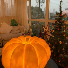 Yellow pumpkin-shaped portable table lamp on coffee table in cozy living room with Christmas decor.