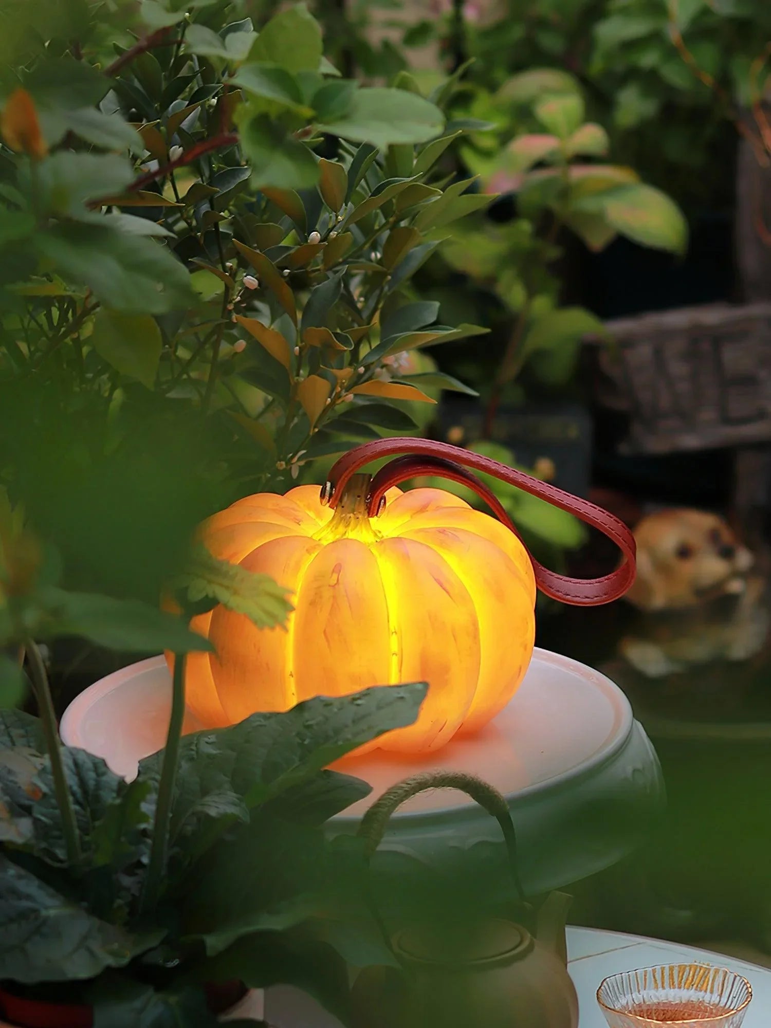 Yellow pumpkin-shaped portable table lamp with handle, glowing on garden table, YH Lamps