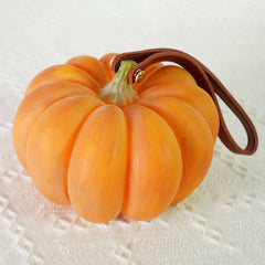 Yellow pumpkin-shaped portable table lamp with leather strap on white textured surface