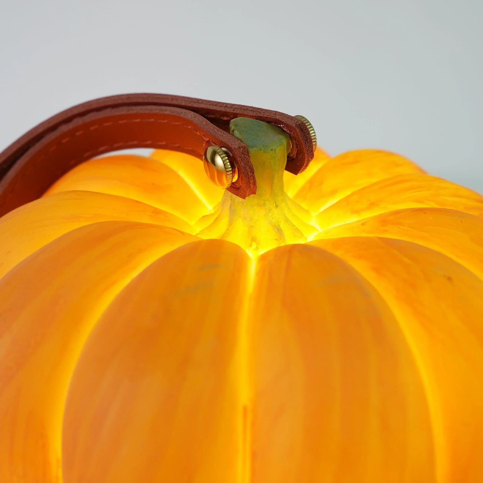 Yellow pumpkin-shaped portable table lamp with leather handle from YH Lamps, glowing softly.