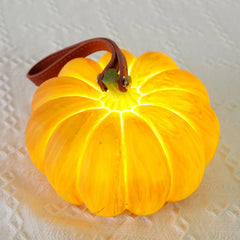 Yellow pumpkin-shaped portable table lamp with leather handle on textured white surface
