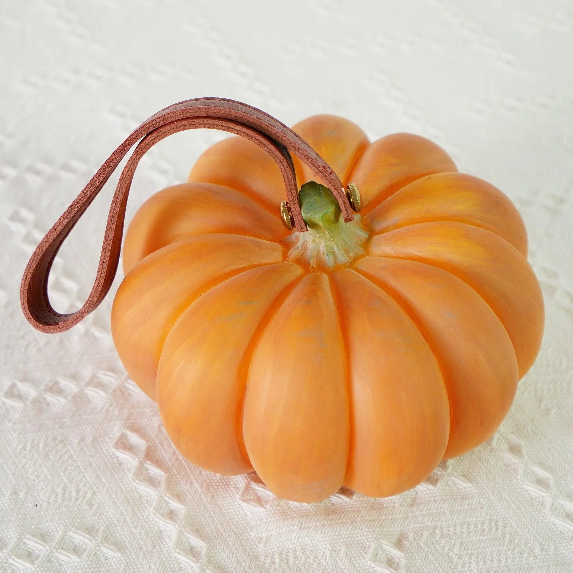 Yellow pumpkin-shaped portable table lamp with brown leather handle on white textured surface