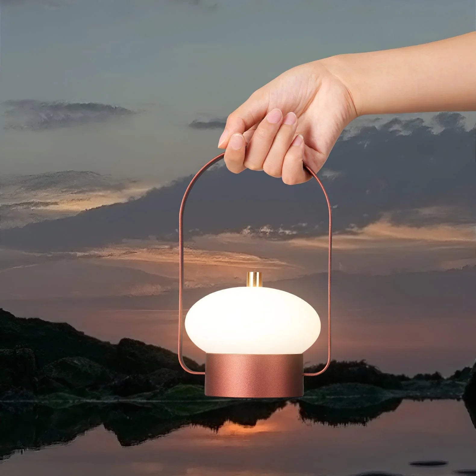 Hand holding modern dark red portable YH Lamps table lamp with soft glow outdoors at sunset
