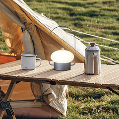 Modern portable table lamp with soft white light on outdoor wooden table beside enamel mug and coffee pot, YH Lamps