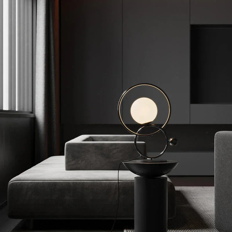 Modern double ring designer table lamp with glowing orb on black stand in contemporary living room