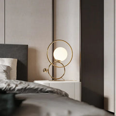 Modern double ring table lamp with gold finish and white globe shade on bedside table