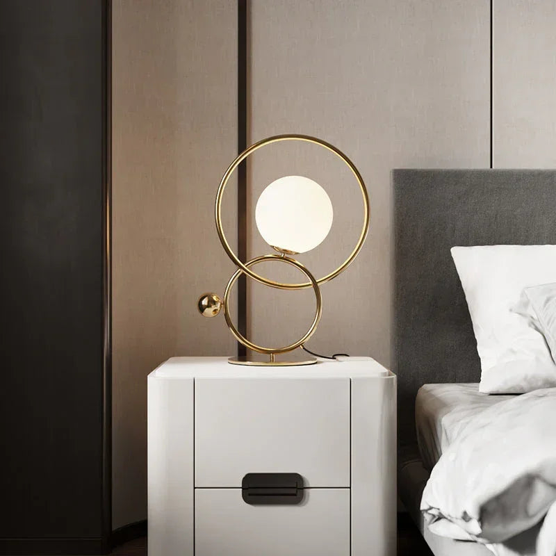 Modern gold double ring table lamp with white globe on nightstand beside bed, YH Lamps