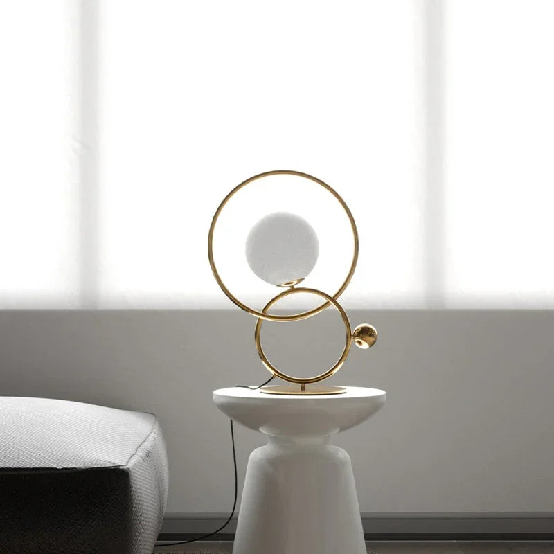 Modern gold double ring designer table lamp with white globe, featured on a white pedestal