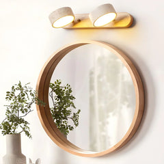 Modern walnut color 2-light wall lamp above round wooden framed mirror with green plant in white vase