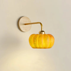 Yellow gold pumpkin-shaped wall lamp with brass fixture on neutral wall, modern lighting