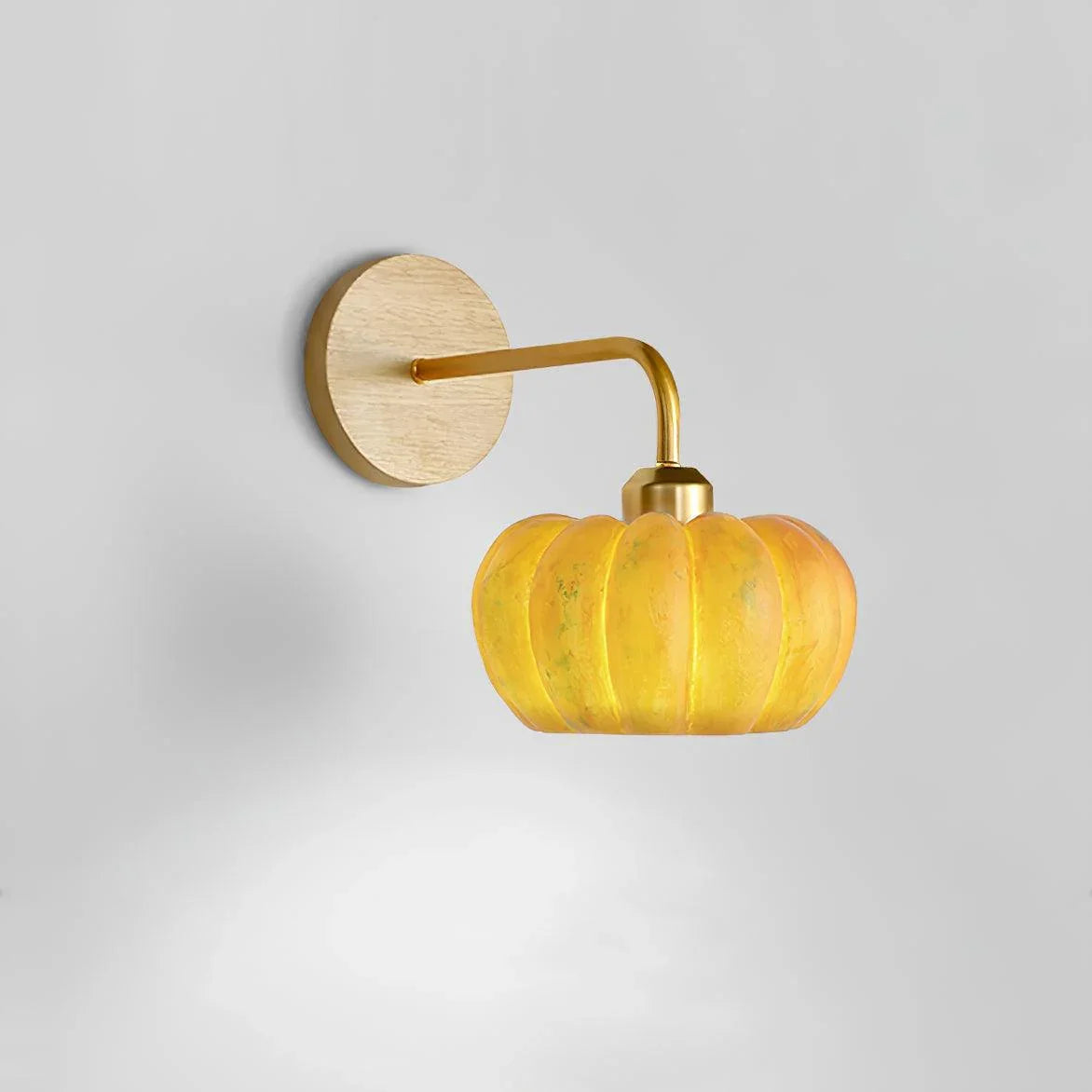Modern yellow gold pumpkin wall lamp with glass shade and brass mount on white wall