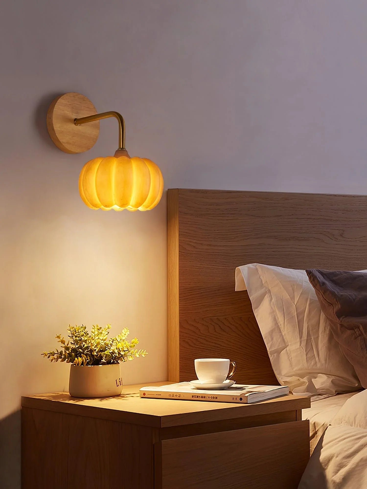 Yellow gold pumpkin wall lamp above modern wooden bedside table with plant and cup