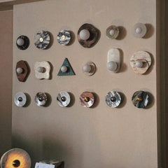 Modern marble wall lamps in various shapes and colors displayed on a beige wall at YH Lamps