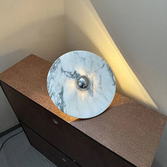 Modern marble wall lamp with chrome accent and warm light on a wooden cabinet