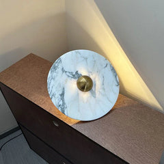 Modern marble wall lamp with brass center on a wooden cabinet, warm ambient lighting