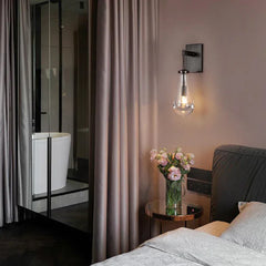 Modern raindrop glass wall sconce in bedroom, above bedside table with pink flowers, YH Lamps