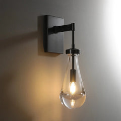Modern raindrop glass wall sconce with black metal mount, illuminated on a grey wall