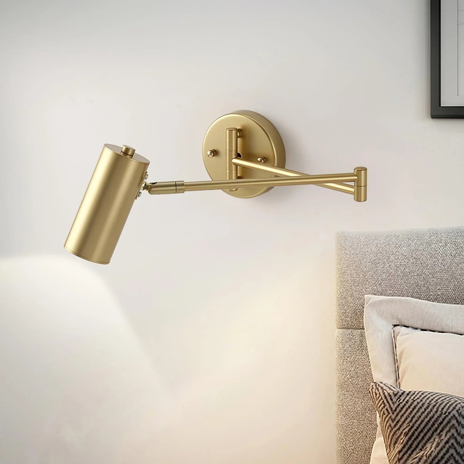 Gold swing arm wall sconce with warm light, mounted beside a textured grey upholstered bed