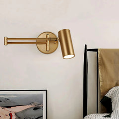 Modern gold swing arm wall sconce with warm light above a bed and framed art in a bedroom