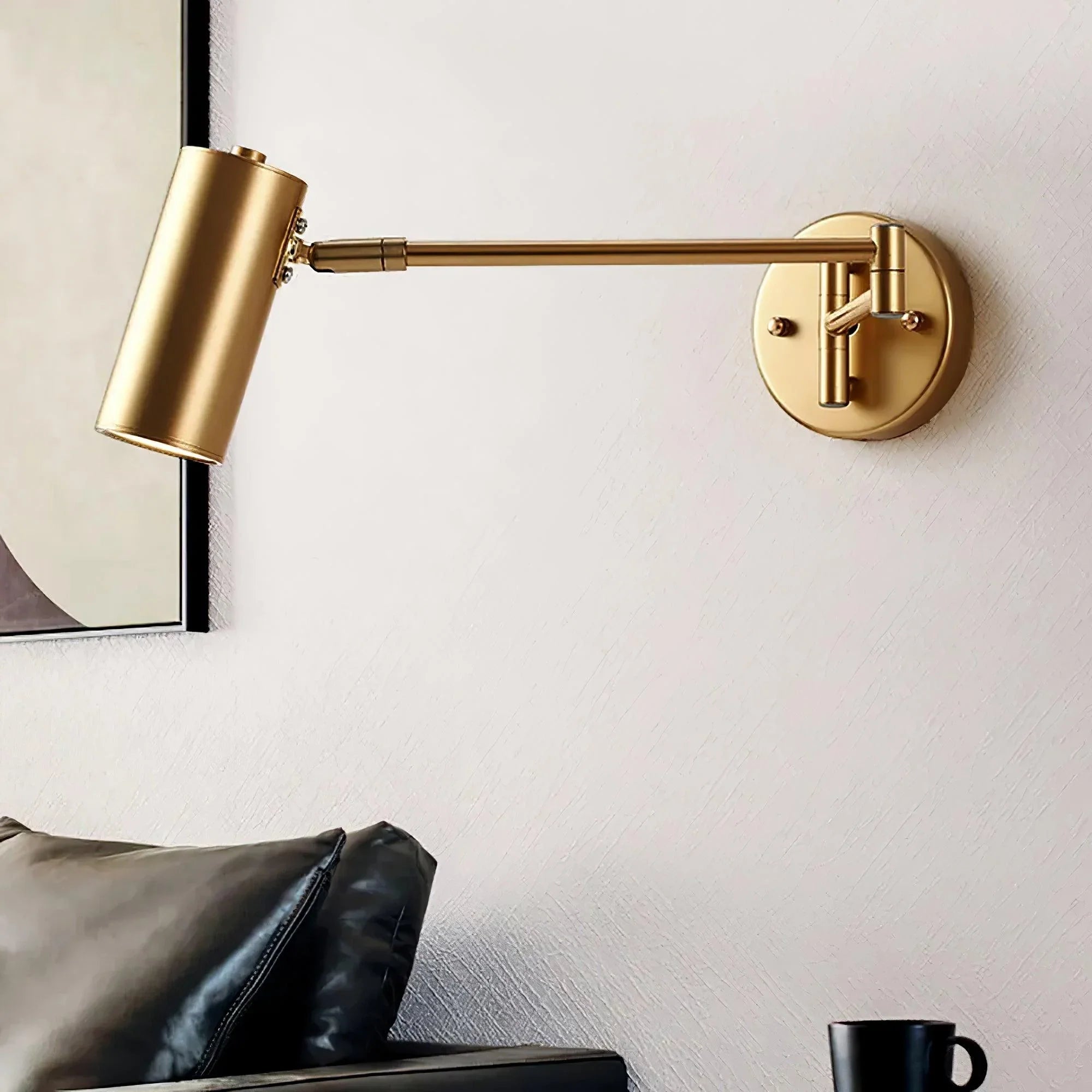 Modern gold swing arm wall lamp with warm light mounted above black leather sofa and black coffee mug