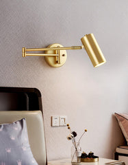 Modern gold swing arm wall lamp with warm light above bedroom side table with decor