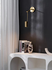 Modern gold swing arm wall sconce above white console table with art books and sculpture, black wall backdrop