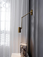 Modern gold swing arm wall lamp with adjustable arm and warm light above white side table with books and sculpture