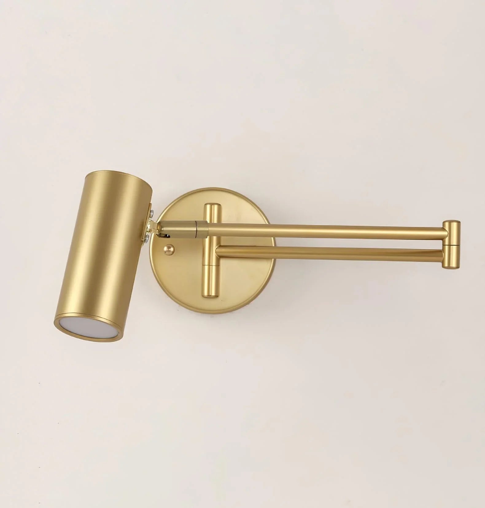 Gold-colored modern swing arm wall lamp with cylindrical shade and wall switch on white background