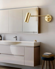 Modern bathroom with gold swing arm wall sconce, white sink vanity, and folded towels on stool