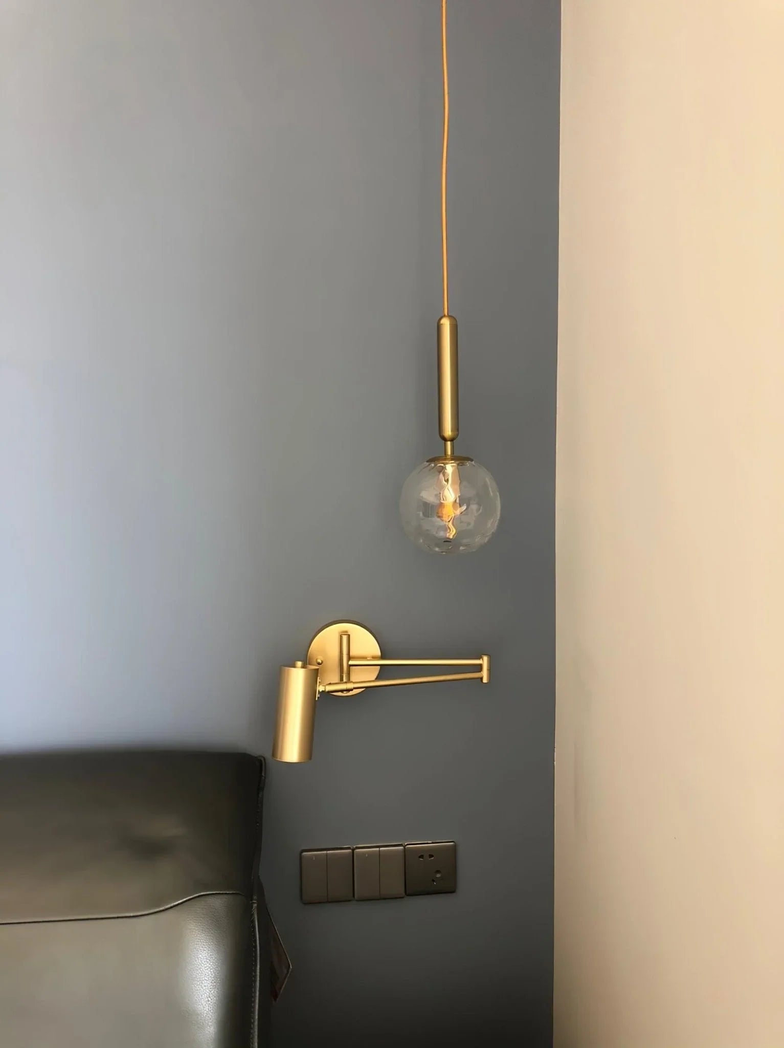 Modern gold adjustable swing arm wall lamp and hanging pendant with clear globe bulb on blue and beige wall