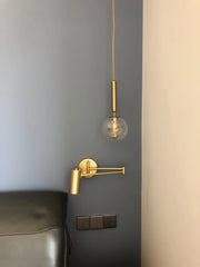 Modern gold adjustable swing arm wall lamp and hanging pendant with clear globe bulb on blue and beige wall