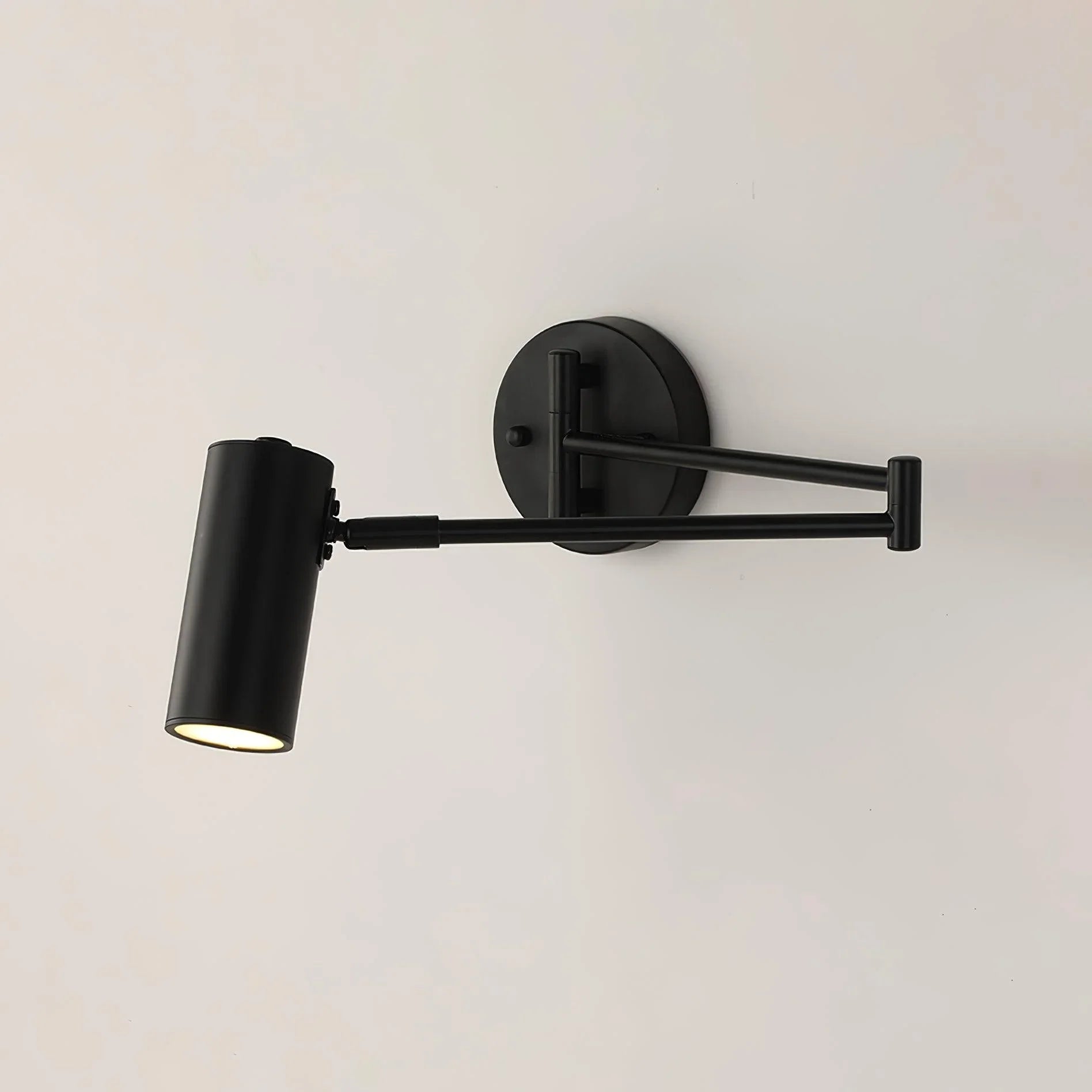 Modern black swing arm wall sconce with adjustable cylindrical shade and warm light on white wall
