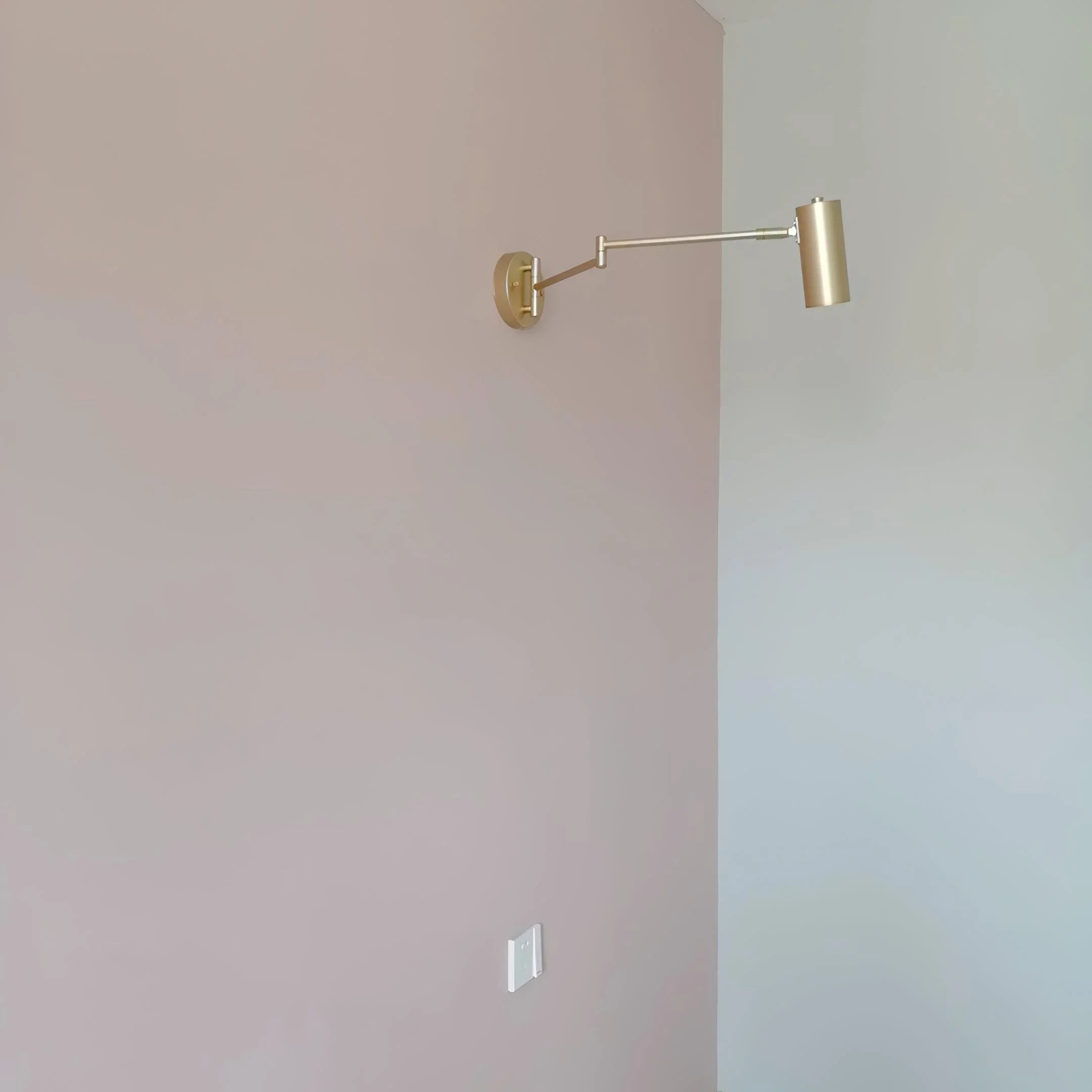 Modern gold swing arm wall lamp with wall switch on pink and white wall