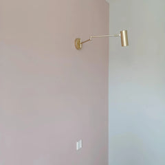 Modern gold swing arm wall lamp with wall switch on pink and white wall