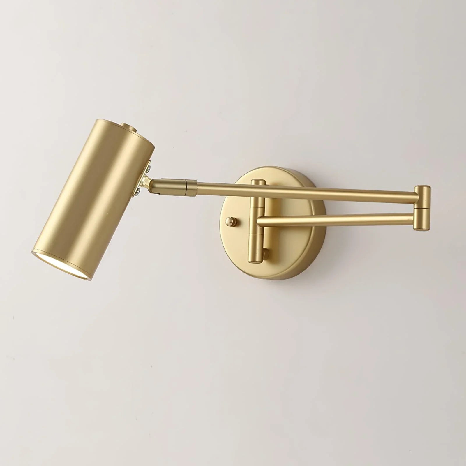 Modern gold swing arm wall lamp with cylindrical shade and warm light, mounted on white wall