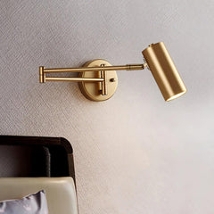 Gold swing arm wall sconce with adjustable cylindrical shade and wall switch, mounted above a bed