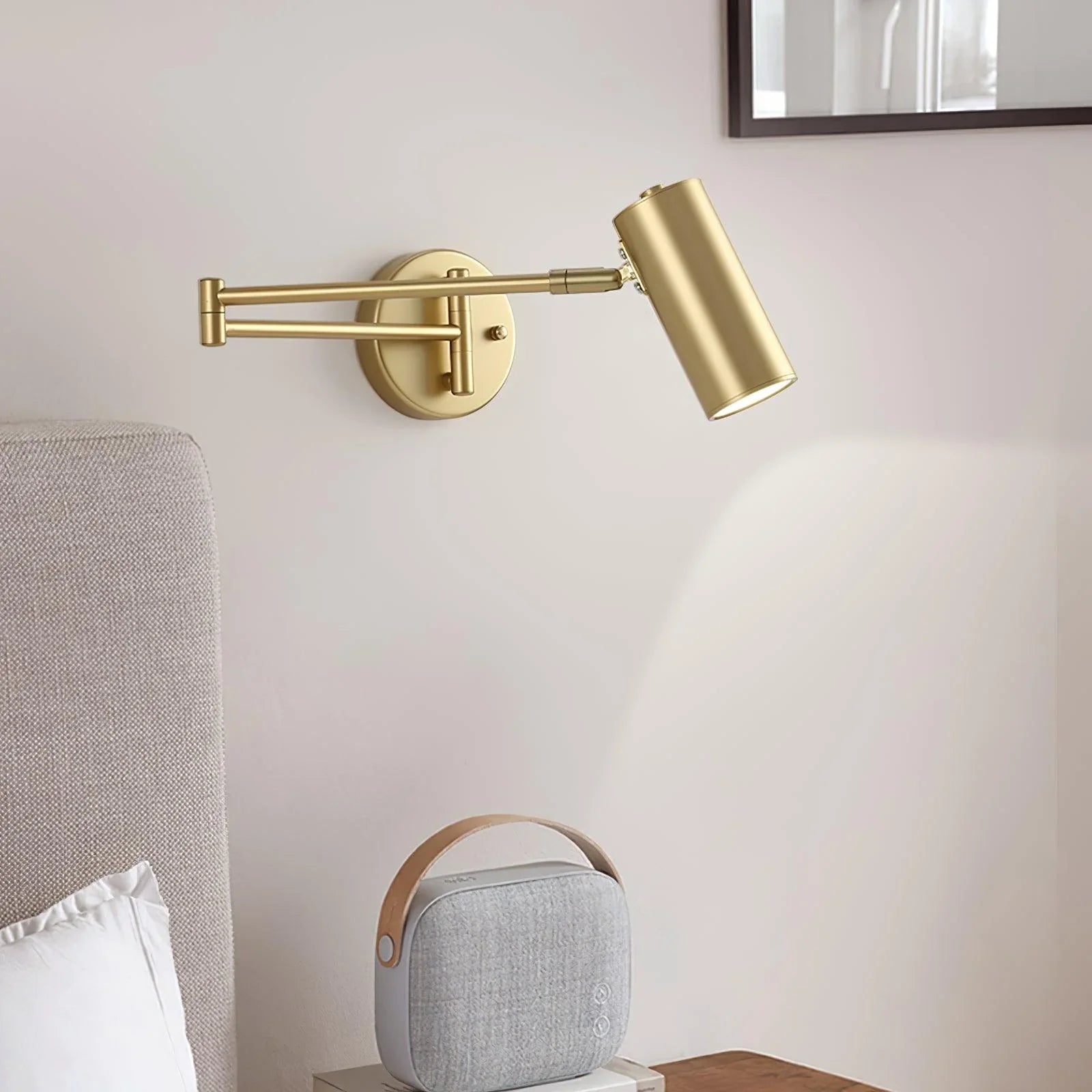 Modern gold swing arm wall lamp mounted above a bedside table with soft warm light