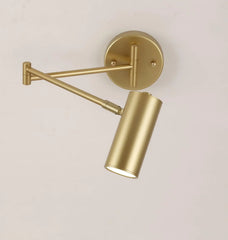 Modern gold swing arm wall lamp with cylindrical shade and wall switch, warm light on neutral wall