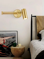 Gold swing arm wall lamp above wooden side table with green mug and white bubble candle, next to bed with patterned bedding