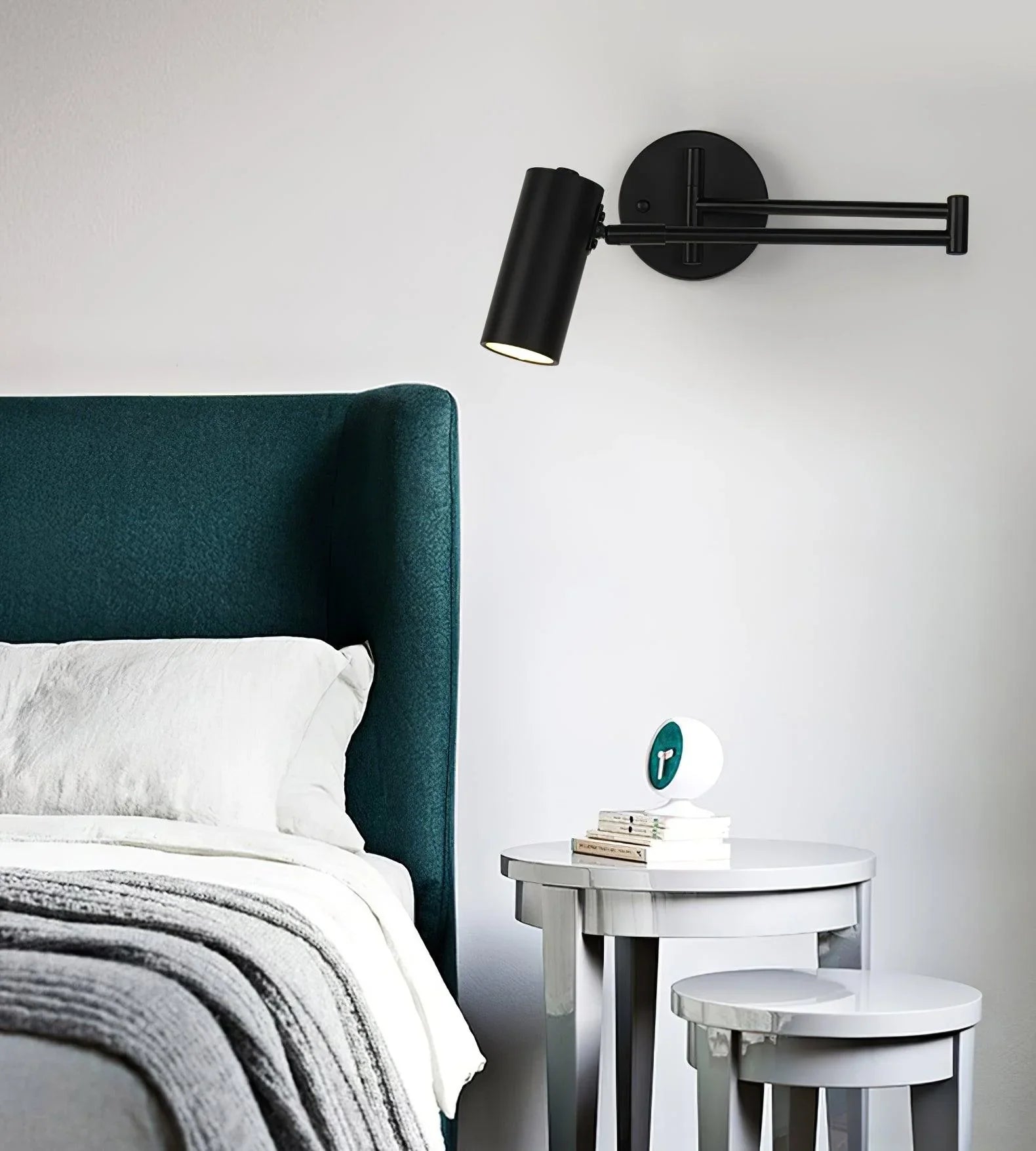 Modern black swing arm wall sconce above white nested bedside tables with books and clock