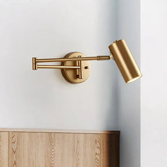 Gold swing arm wall sconce with warm light mounted on white wall above wooden surface