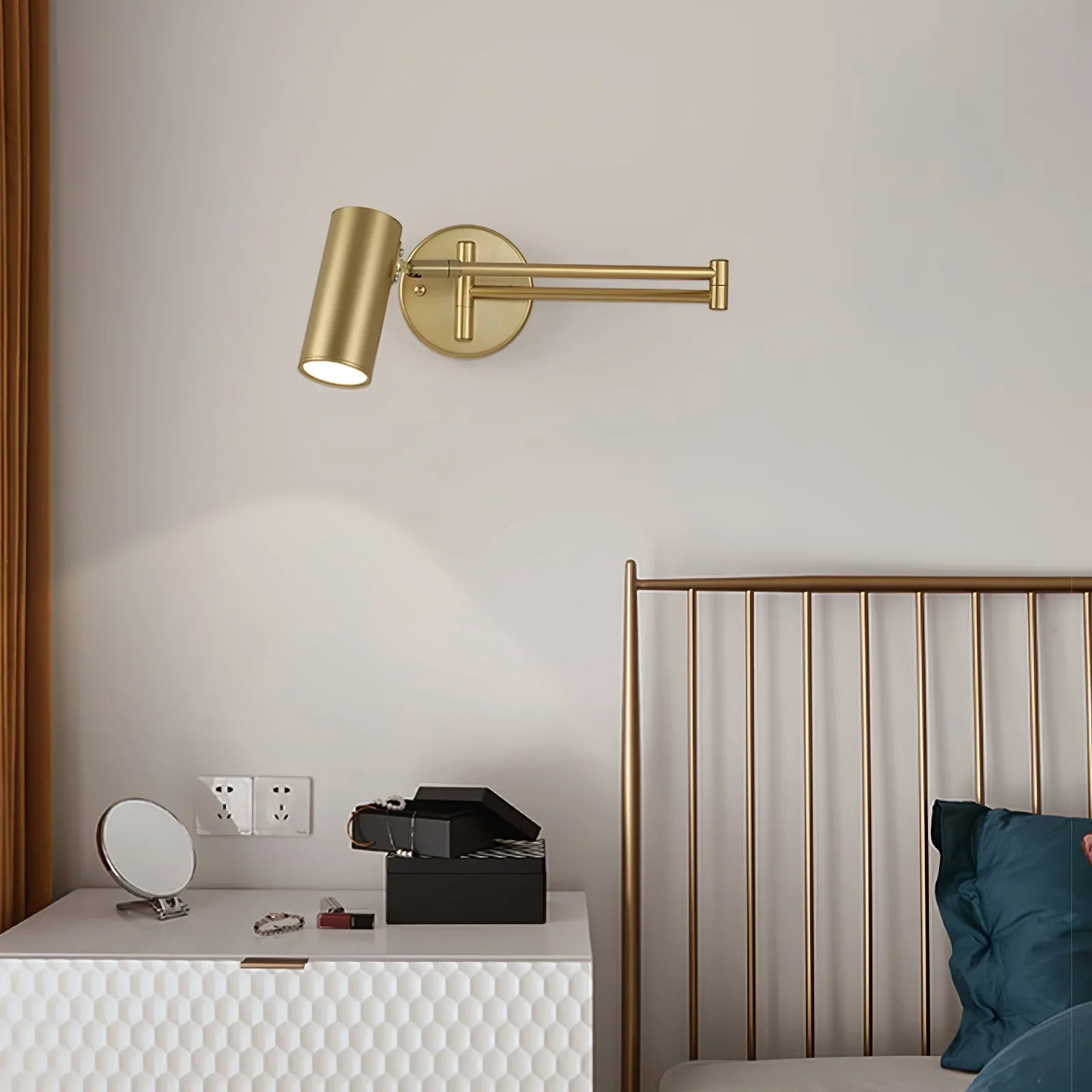 Gold swing arm wall lamp with warm light above white bedside table and gold metal bed frame in modern bedroom