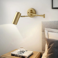 Modern gold swing arm wall lamp above wooden nightstand with cup and books in cozy bedroom