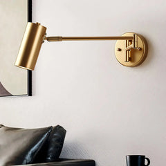 Modern gold swing arm wall lamp with warm light above black leather sofa and coffee cup