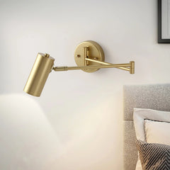 Gold swing arm wall lamp with warm light mounted beside a bed with cushions in a modern bedroom