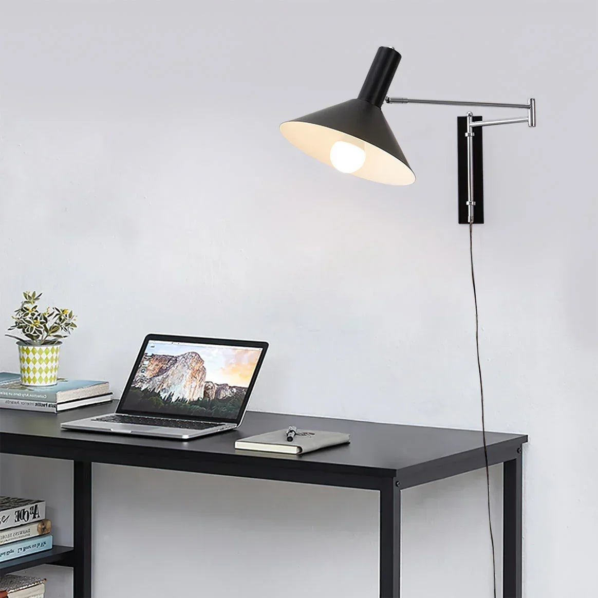 Modern black wall lamp with adjustable arm above minimalist desk workspace